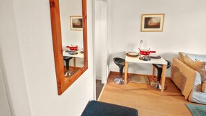 A compact living space with a dining area, a sofa, and a mirror reflecting the room.