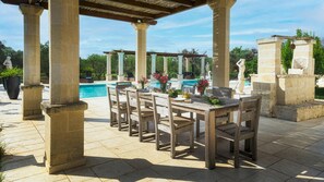 An outdoor patio with a pool, stone columns, and a wooden table set for dining. - Villa La Dolce Vita 6 Emma Villas (Oria)