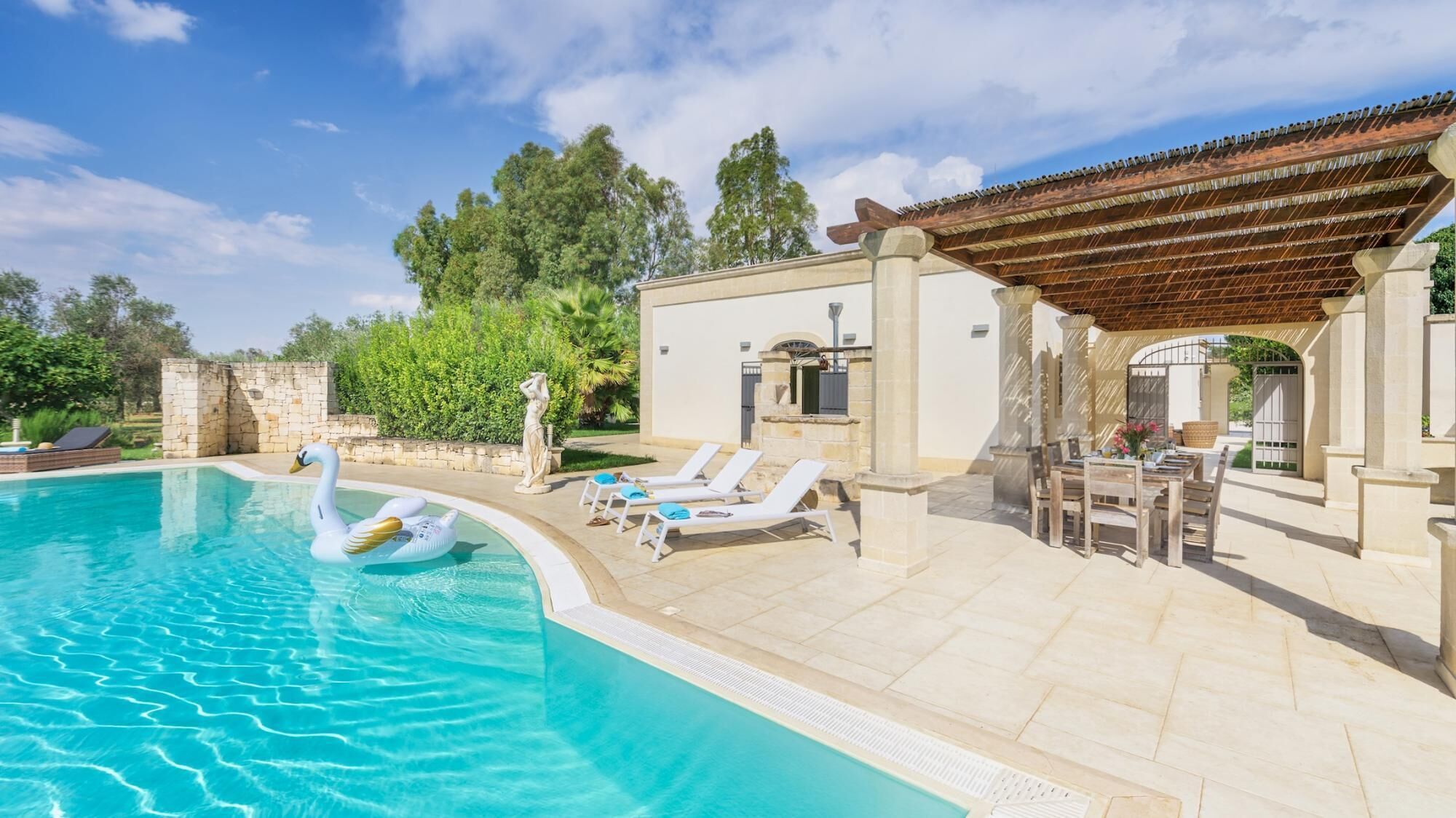 Une piscine avec des chaises longues, une pergola et un mur en pierre.
