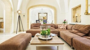 A spacious living room with a large brown sectional sofa, a wooden coffee table with a glass dome centerpiece, and a tripod floor lamp.