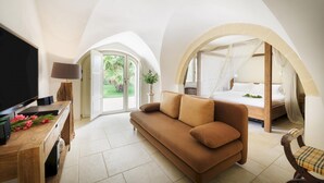 A modern hotel room with a large bed, a sofa, a TV, and a balcony with a view of the garden.