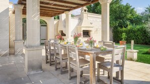 An outdoor patio with a wooden table and chairs, surrounded by stone pillars and a pergola.