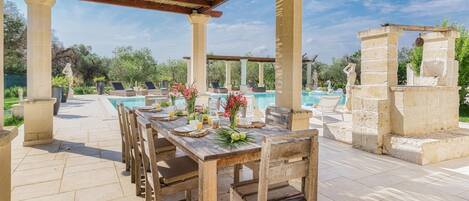 An outdoor dining area with a pool and statues in the background.