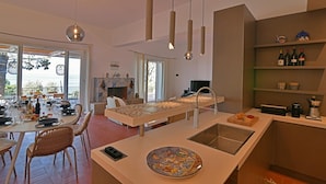A modern kitchen with a central island, a dining area with wicker chairs, and a view of the sea. - Villa Salone 8 Emma Villas (Pollina)