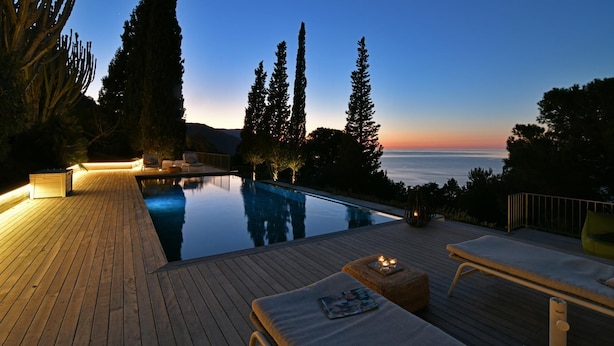 A serene poolside area with wooden decking, lounge chairs, and a view of the ocean at dusk. - Villa Salone 8 Emma Villas (Pollina)