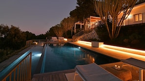 A swimming pool with a wooden deck and lounge chairs, surrounded by trees and a building with a staircase. - Villa Salone 8 Emma Villas (Pollina)
