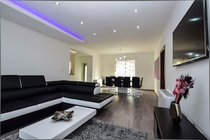 Uma sala de estar moderna com um sofá seccional preto, uma mesa de centro branca e uma área de jantar com lustre.
