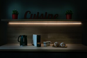 En træbordplade med elkedel, kaffemaskine, to kopper og et fad med kager.