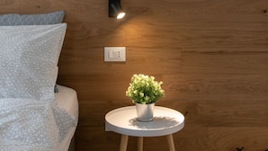 A bed with patterned bedding, a small white table with a potted plant, and a wall-mounted light fixture. - C-Apartment A Scrovegni luxury suite (Padova)