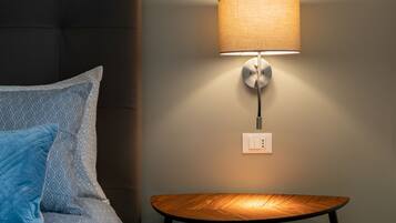 Una cama con almohadillas estampadas, una mesa redonda de madera y una lámpara fijada a la pared.