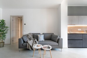 En moderne stue med en grå sofa, et lille sofabord og et tilhørende bord. En potteplante er synlig på venstre side.