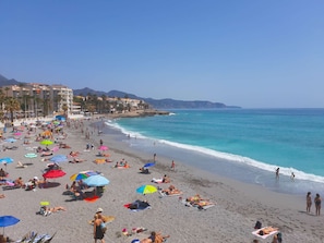 Une plage bondée où l’on voit des gens bronzer et se baigner, des parasols et des bâtiments en arrière-plan.