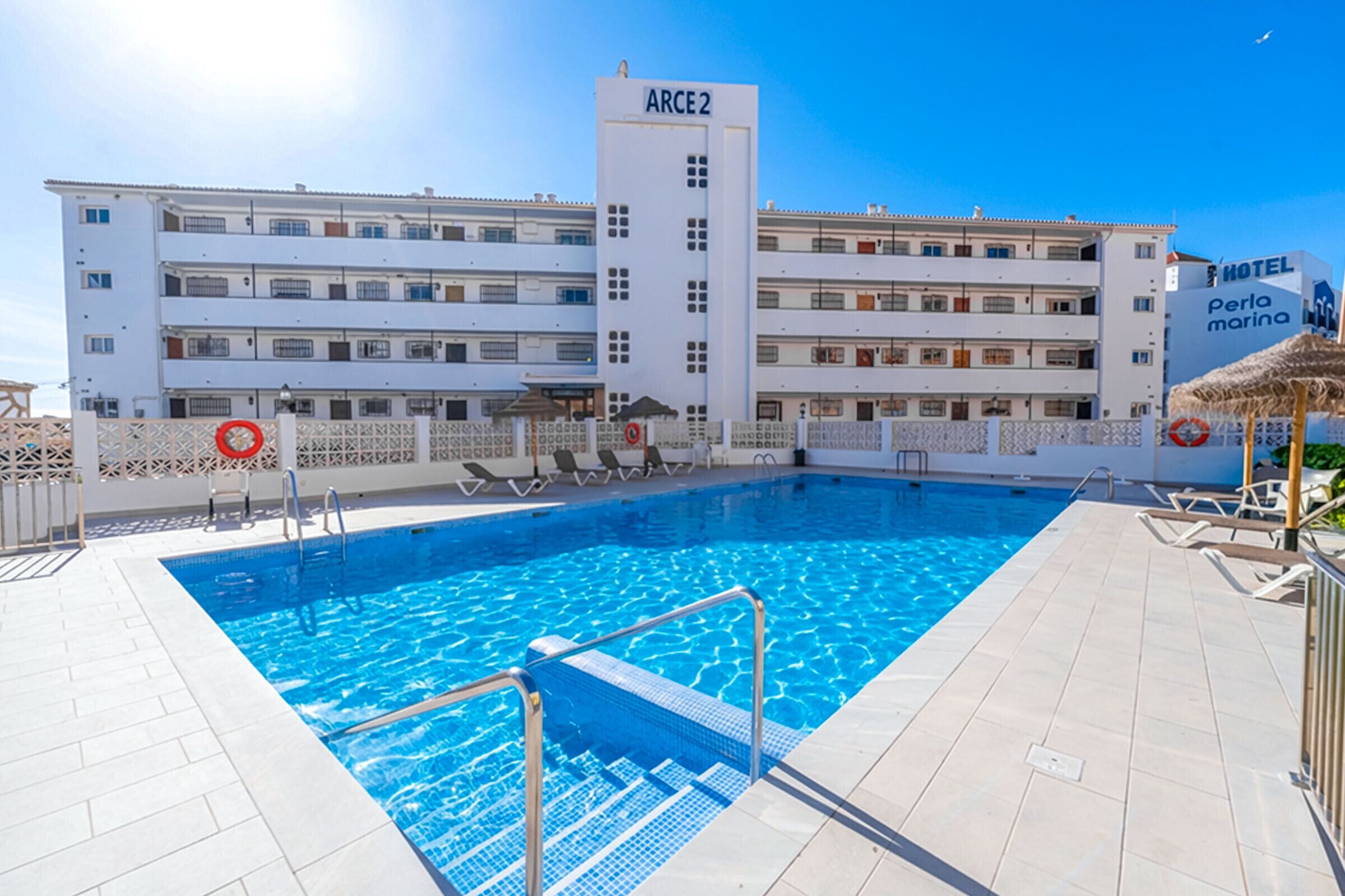 Ein Hotel mit Schwimmbad, Rettungsturm und Strandsonne.