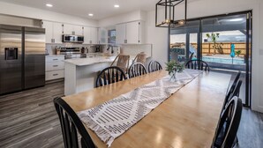 Een moderne keuken met witte kasten, roestvrijstalen apparatuur en een eethoek met een houten tafel en stoelen.
