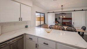 Een moderne keuken met witte kasten, een marmeren aanrechtblad en een eethoek met rieten stoelen en een houten tafel.