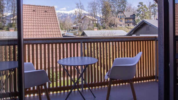 En balkon med gelænder i træ, to hvide stole og et bord.
