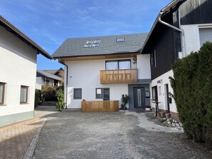 Une maison moderne à deux étages, dotée d’un balcon, d’une porte d’entrée et d’un petit jardin.