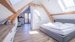 Et moderne loftværelse med skråvægge, træbjælker, en stor seng og udsigt gennem en åben dør.