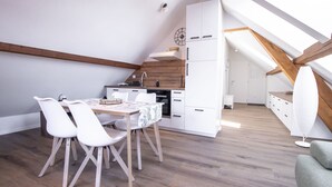 Et moderne køkken med hvide skabe, trælofter og et spiseområde med hvide stole og et bord.