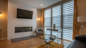 Una sala de estar moderna con chimenea, un televisor de pantalla plana montado en la pared, una mesa de centro de vidrio y un sofá.