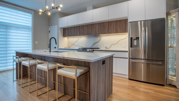 Una cocina moderna con una isla central, taburetes de bar, electrodomésticos de acero inoxidable y armarios de madera.