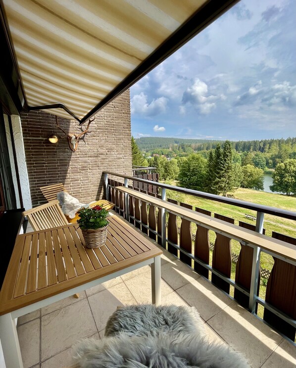 A balcony with a wooden table, a potted plant, and a fur rug.