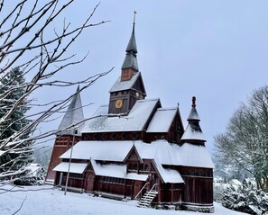 A traditional wooden church with a tall steeple and a clock tower, surrounded by snow-covered trees.