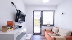Uma sala de estar moderna com um sofá, uma televisão na parede e uma janela com persianas.