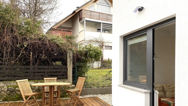 Um pátio com mesa e cadeiras de madeira, área de cascalho e vista para um edifício residencial com varanda.
