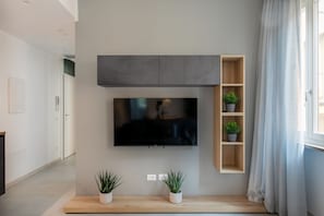 En moderne stue med et fladskærms-tv på væggen, træhylder med planter og et minimalistisk design.