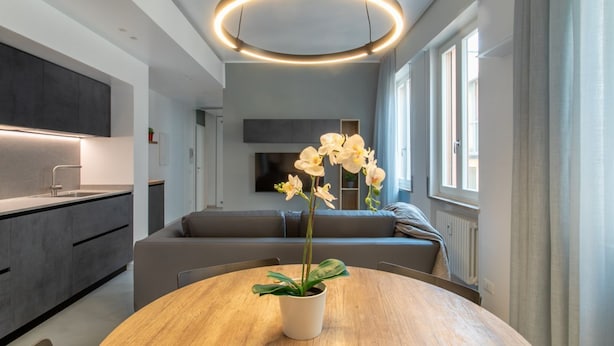 A modern kitchen with a round wooden table, a potted orchid, and a circular light fixture.