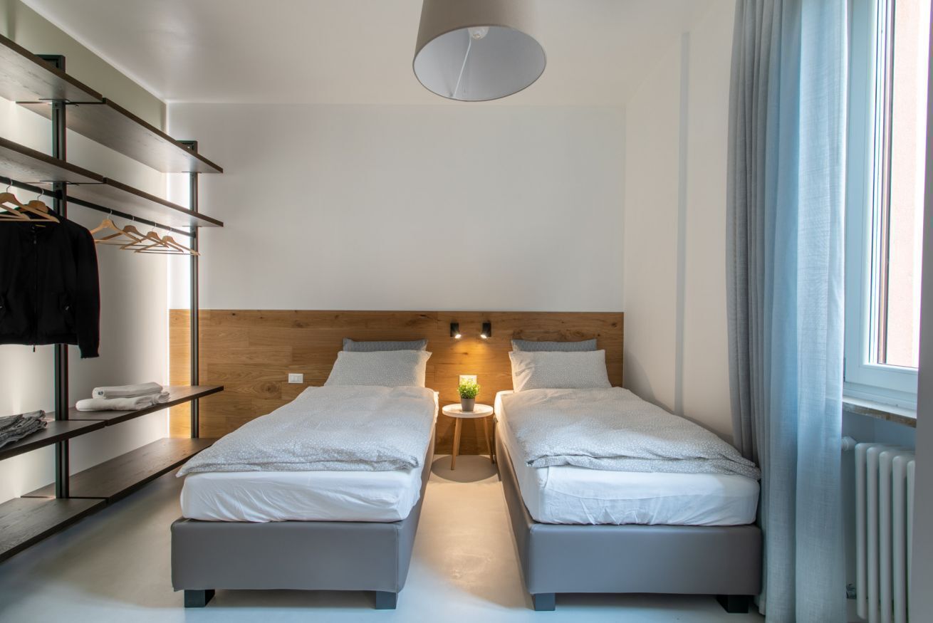 Habitación doble con dos camas, cabecera de madera, repisa con ropa y una mesita con lámpara.