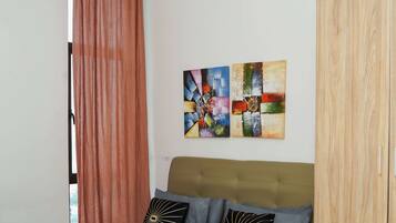 A bedroom with a bed, a wardrobe, a window with curtains, and two wall art pieces.