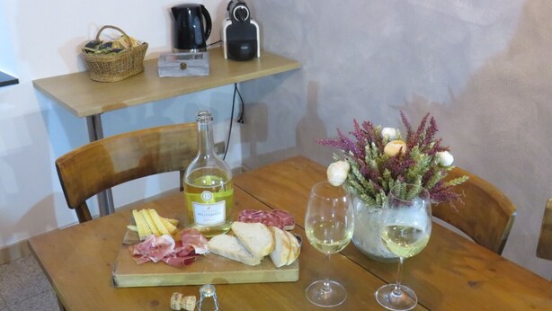 Una mesa de madera con una botella de vino, copas, una tabla de quesos y un ramo de flores.