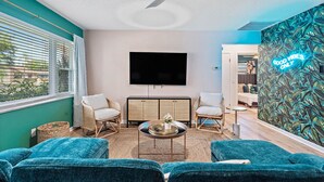 A modern living room with teal walls, a ceiling fan, a flat-screen TV, and a wall with a tropical leaf pattern. - Clearwater Villa / Heated Pool, Hot Tub, Golf! (Clearwater)