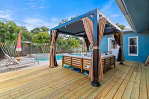 A wooden deck with a covered seating area, a pool, and a house in the background.