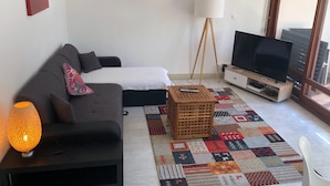 Ett modernt vardagsrum med en soffa, en tv på ett träställ, en lampa och en mönstrad matta.