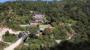 A hillside with several buildings, including a red building with a green roof and a blue building with a green roof. - MANJARI RESORT (Ghansyali)