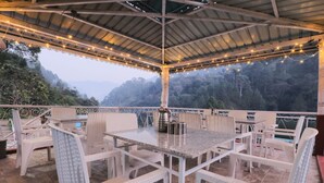 An outdoor patio with white wicker furniture, a metal roof, and string lights. - MANJARI RESORT (Ghansyali)