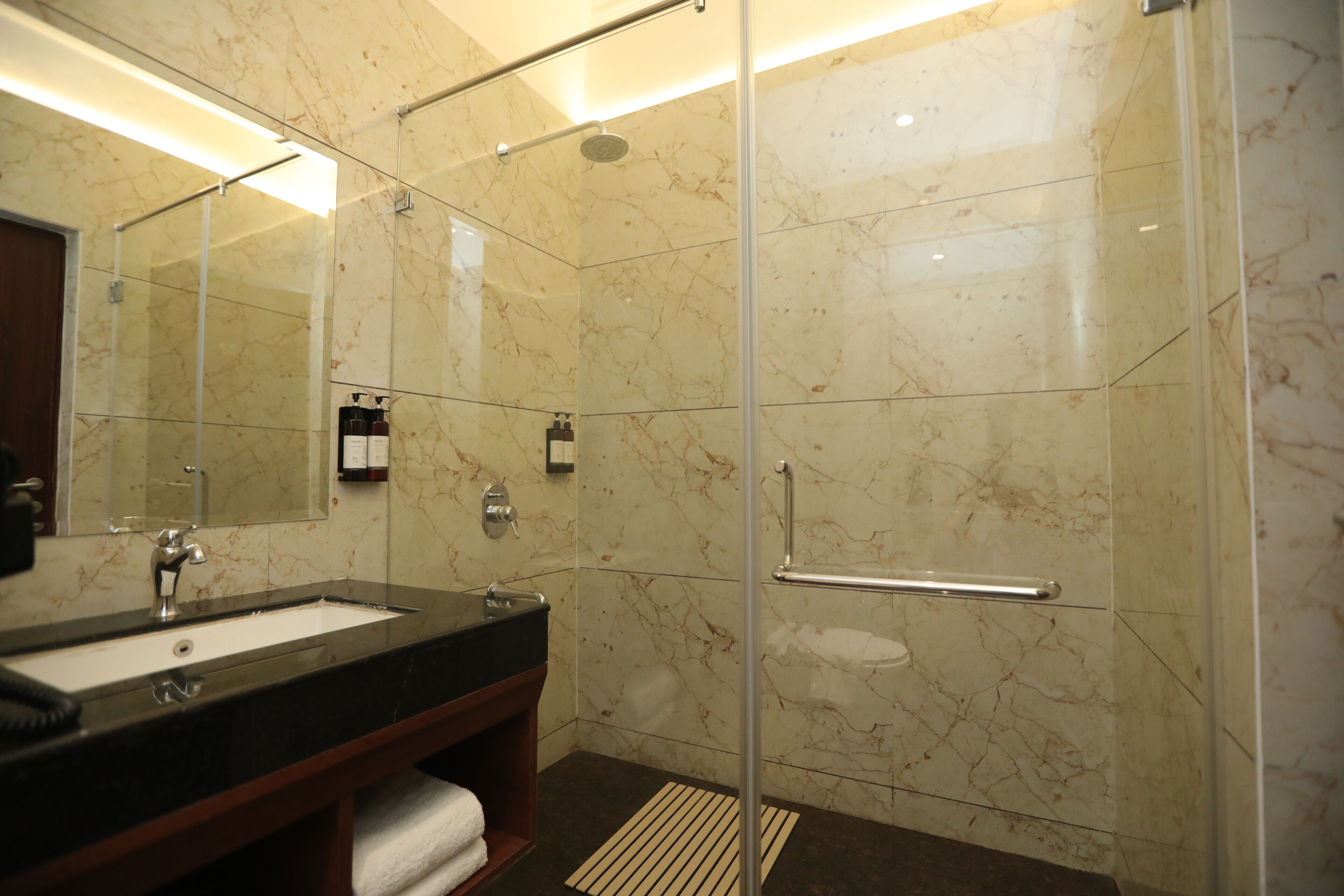 A modern bathroom with a glass-enclosed shower, a marble-tiled wall, and a black sink with a wooden vanity.