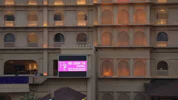 Un immeuble à plusieurs étages doté de fenêtres en arc de cercle et de balcons. Une enseigne indique : « RE:GEN:TA CENTRAL CITY VILAS PALACE BY ROYAL, ORCHID HOTEL LTD. »