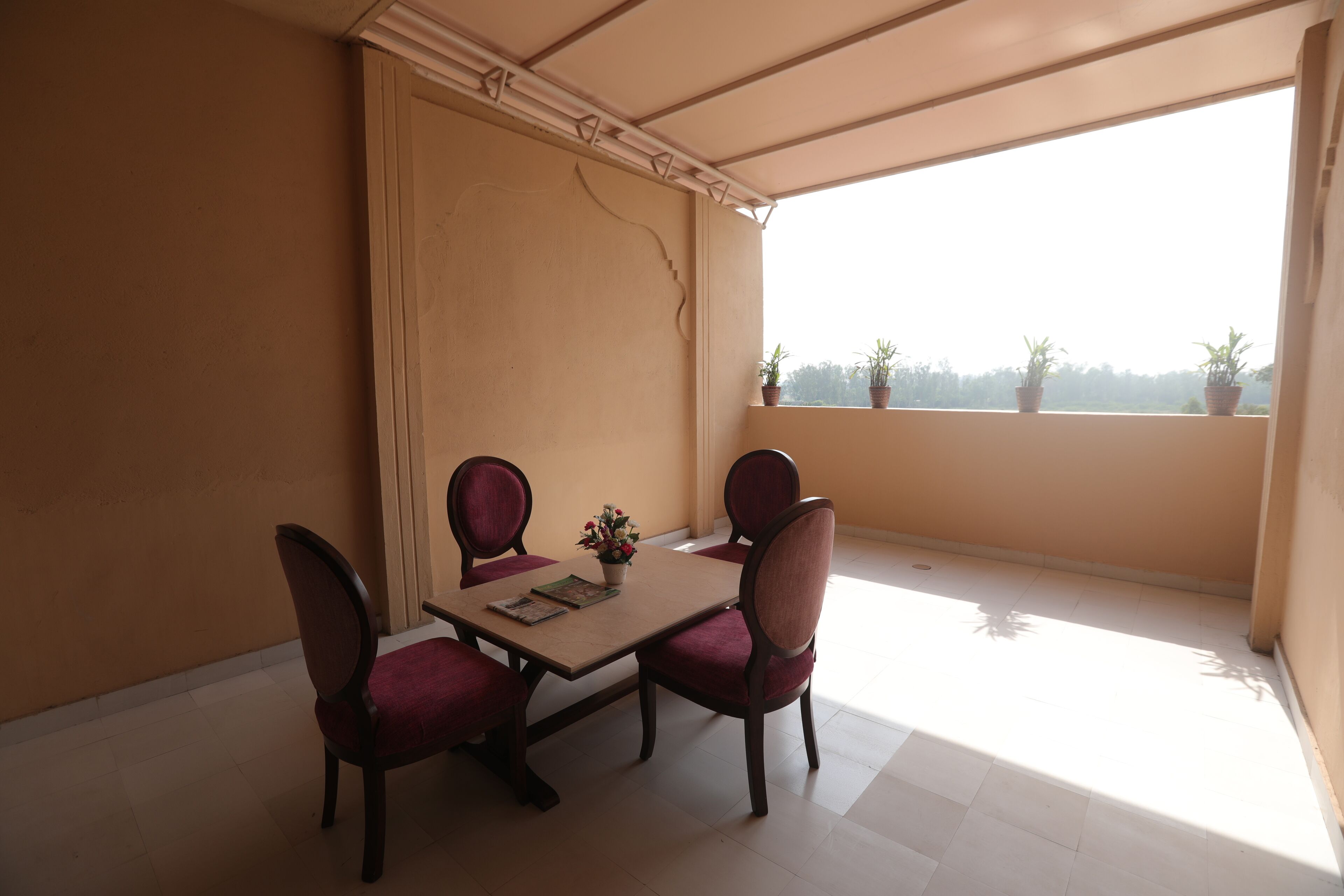 Ein Essbereich mit einem Tisch und vier Stühlen, einer Topfpflanze am Fensterbrett und Blick ins Freie.