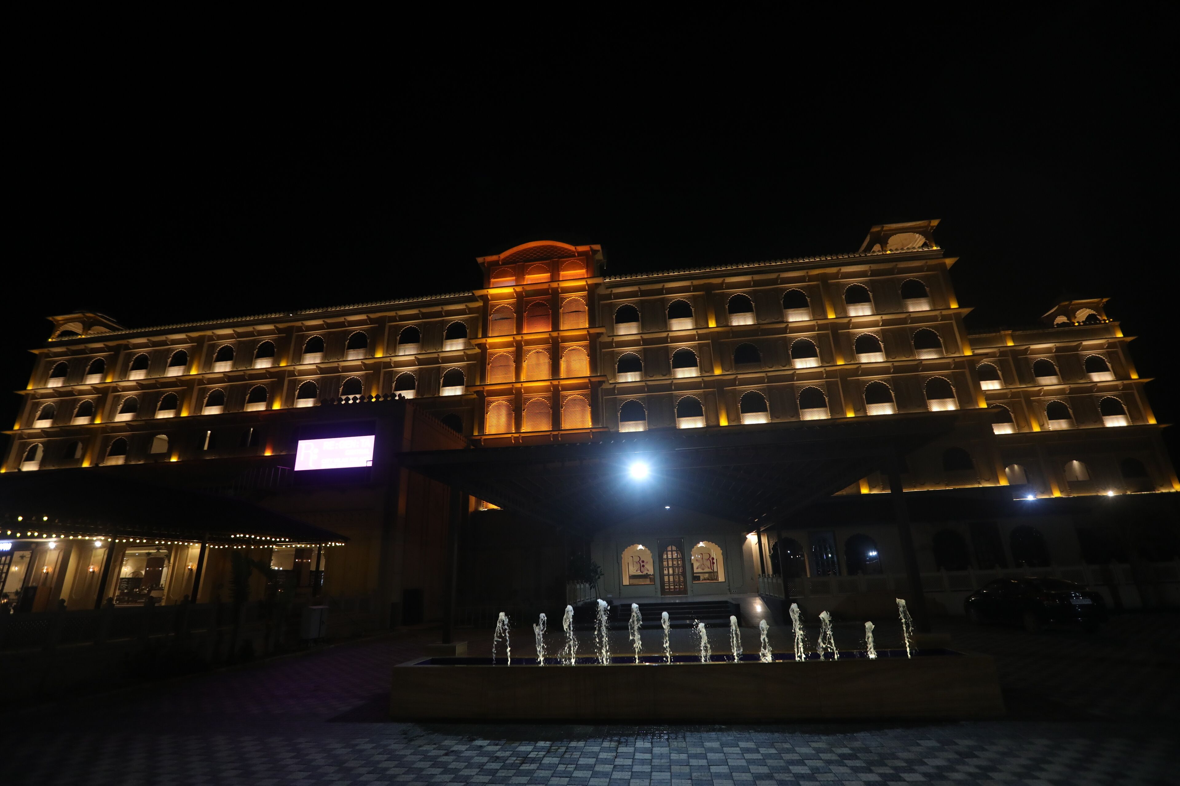 A large hotel with multiple floors, a central fountain, and illuminated windows.