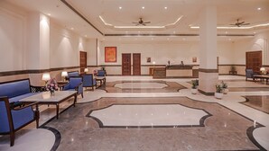 Een ruime lobby met zithoeken, een receptiebalie en plafondventilatoren.