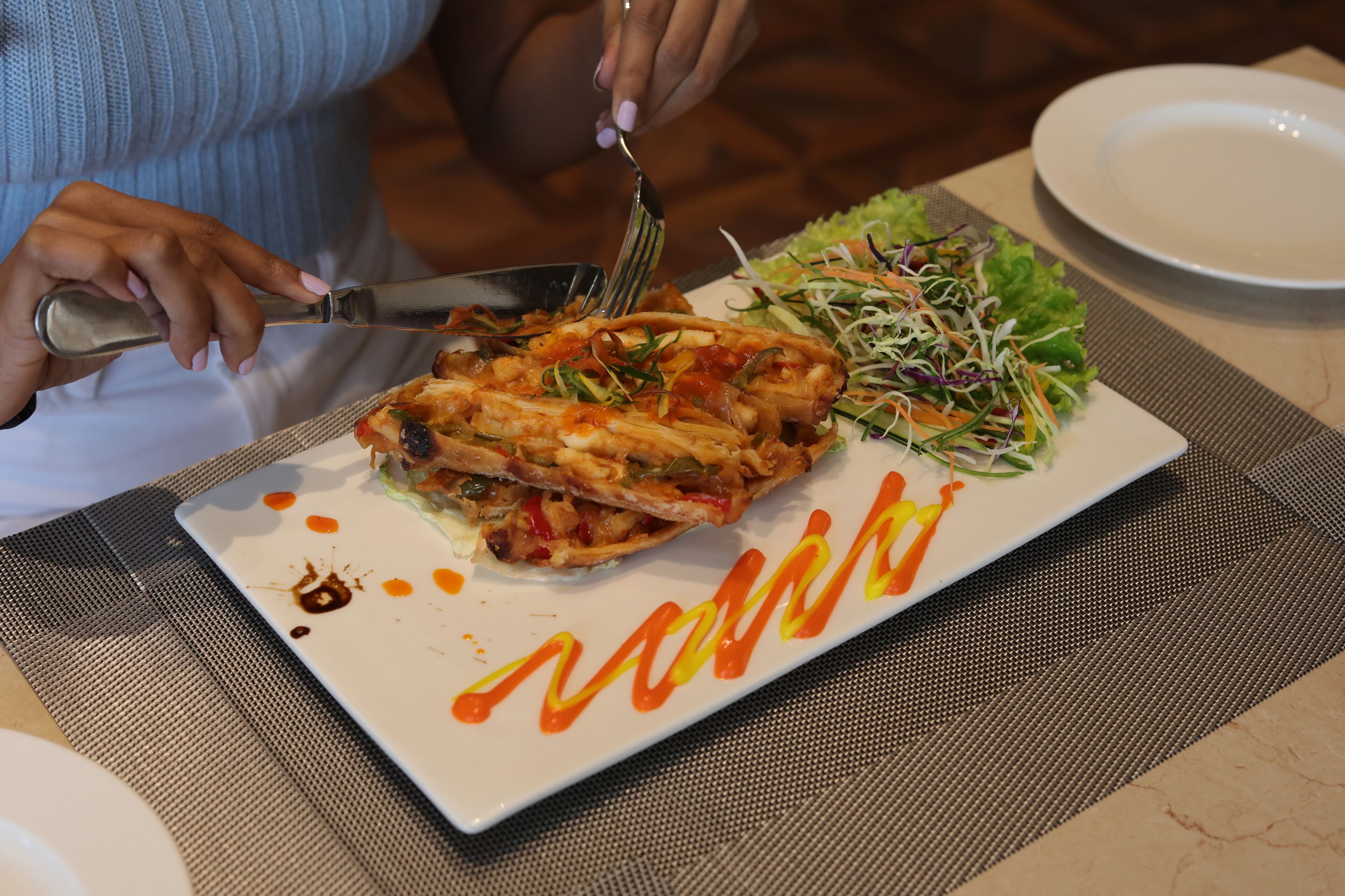 A plate of food with a fork and knife, a salad, and a white plate with a decorative sauce pattern.