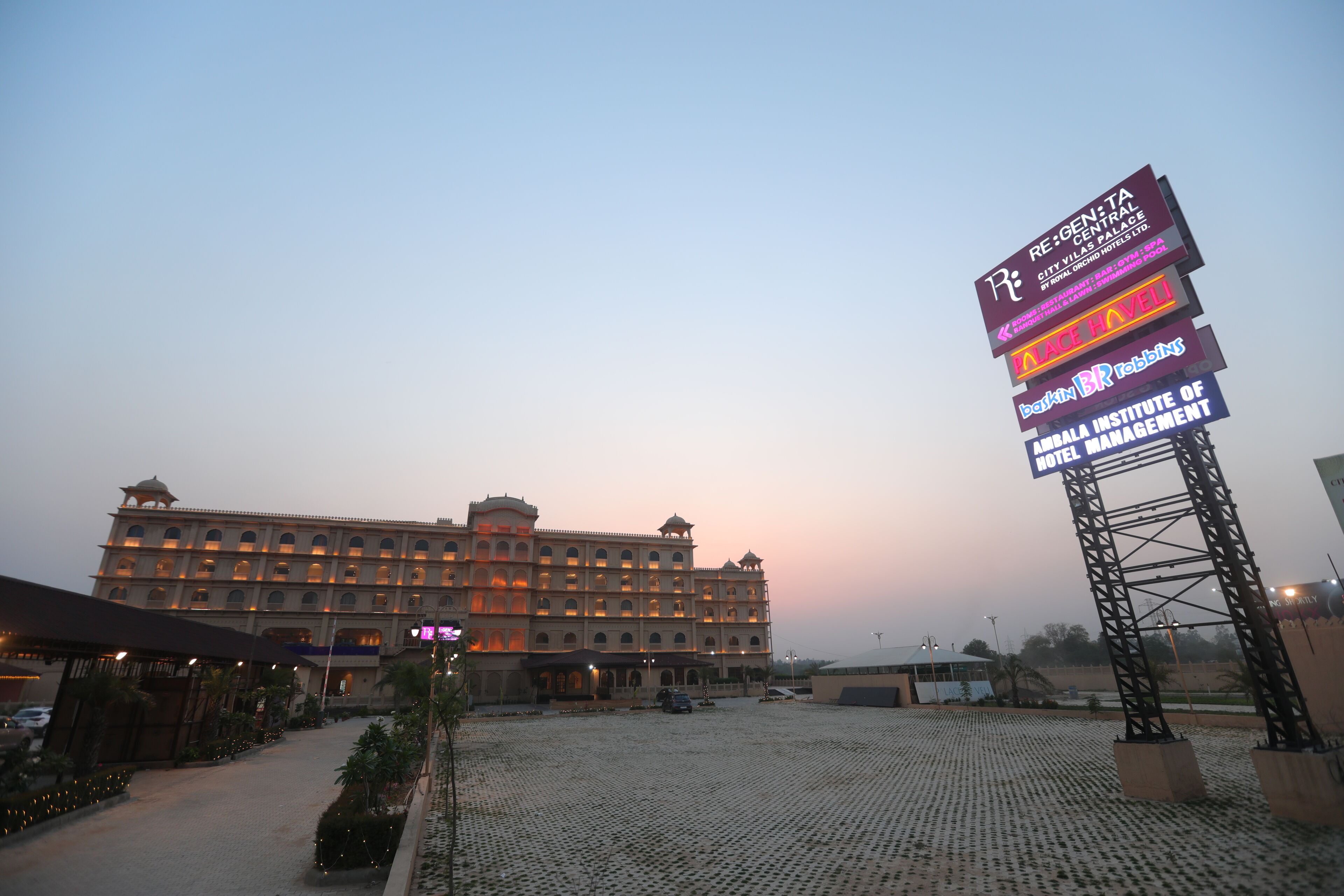 A hotel with a large signboard displaying various amenities and a spacious courtyard.