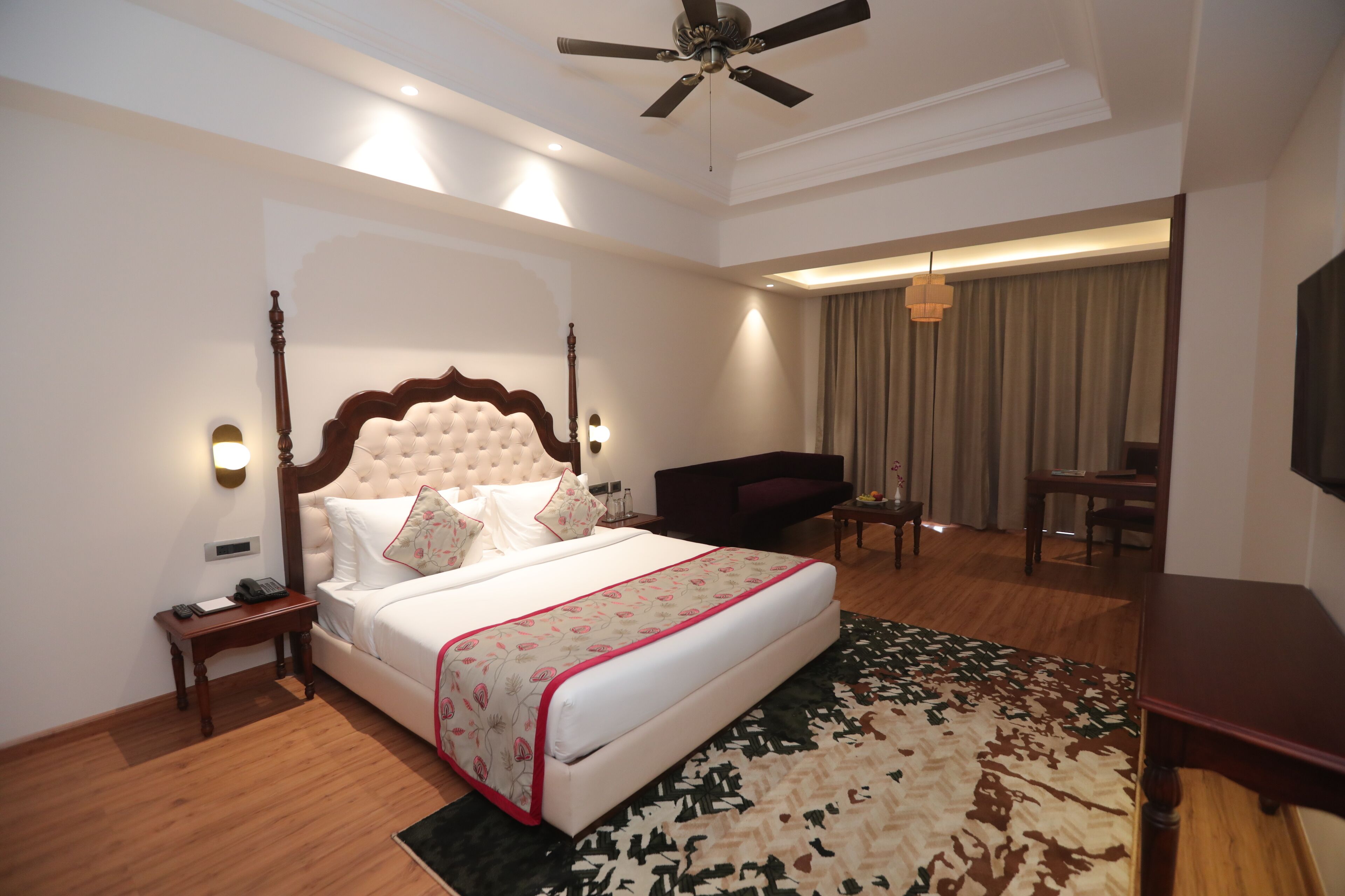 A hotel room with a four-poster bed, a desk, a chair, a television, and a ceiling fan.