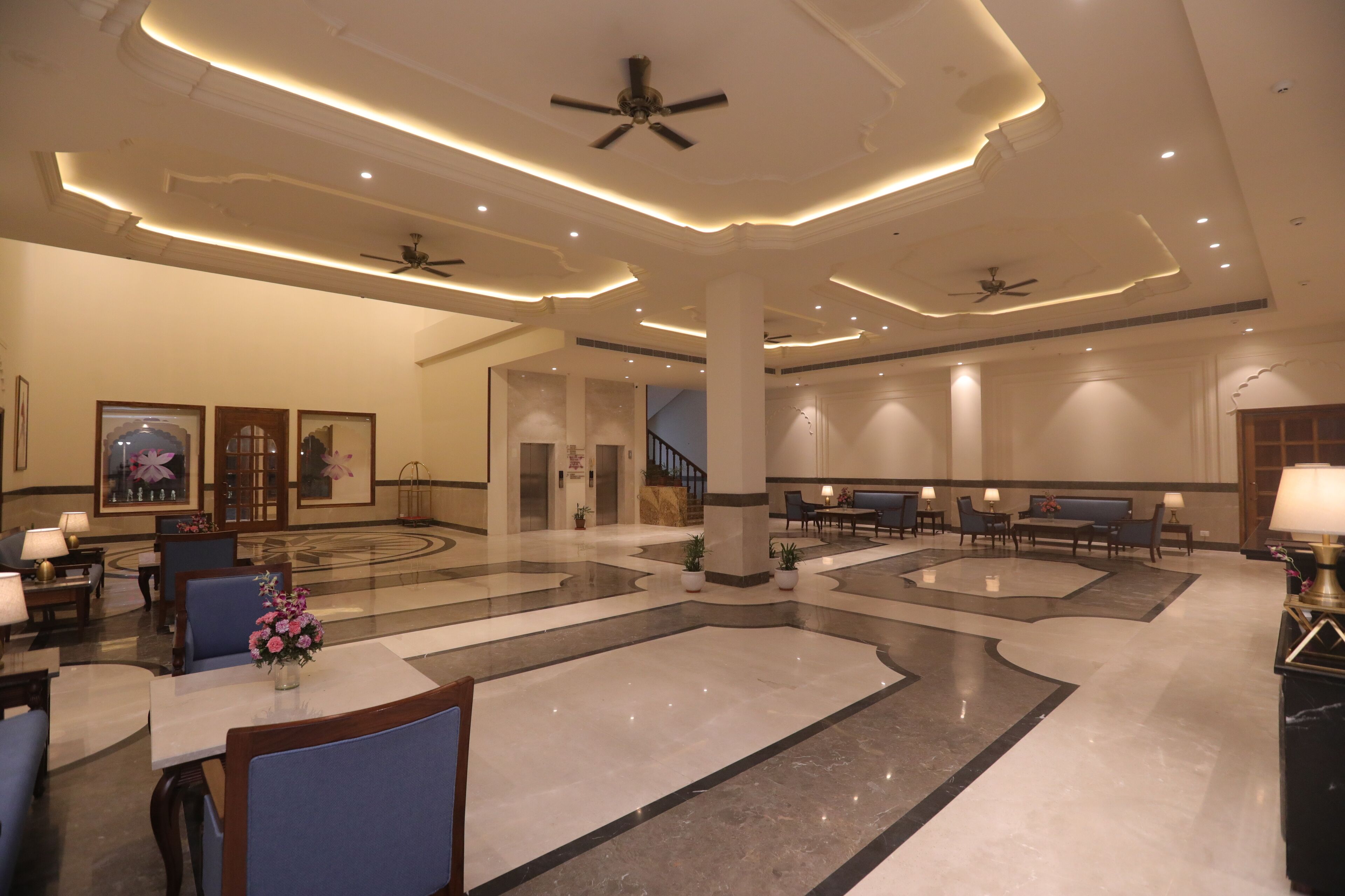 A spacious lobby with a marble floor, seating areas, ceiling fans, and framed artwork on the walls.