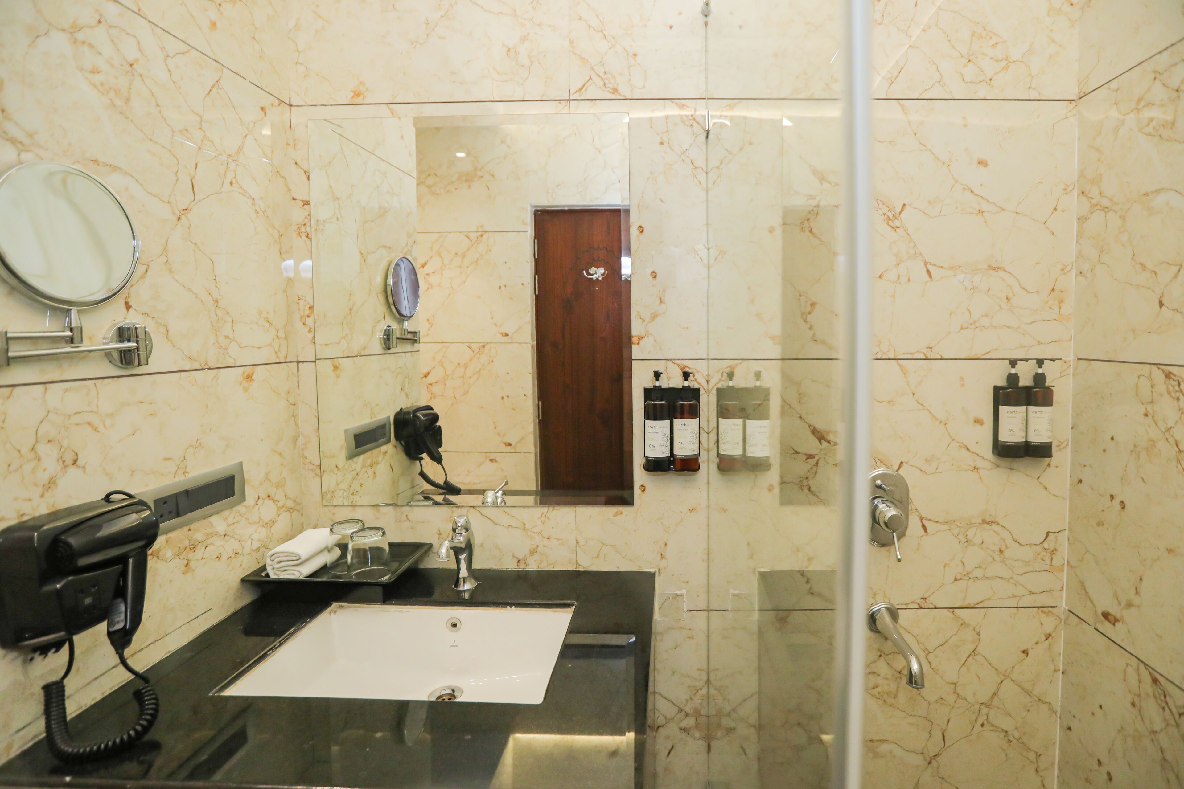 Un baño moderno con pared de mármol, un lavabo con espejo, un secador de pelo y zona de ducha.