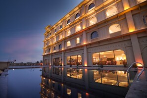 A multi-story building with balconies and large windows, reflecting on a calm water surface below. - Regenta City Villas Palace (Ambala)